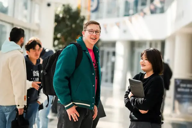 Två personer samtalar i en korridor på campus. Foto.