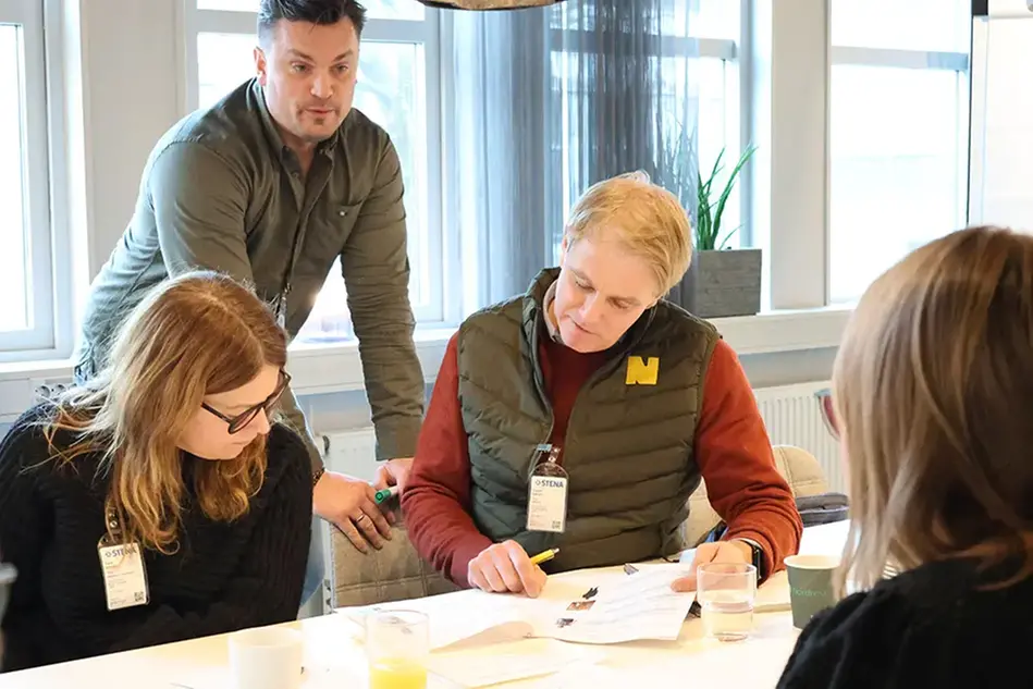 Tre personer samarbetar kring ett papper. Foto