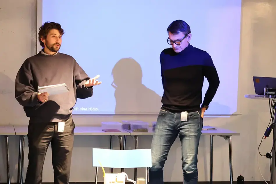 Två män står och presenterar framför en projektor. Foto