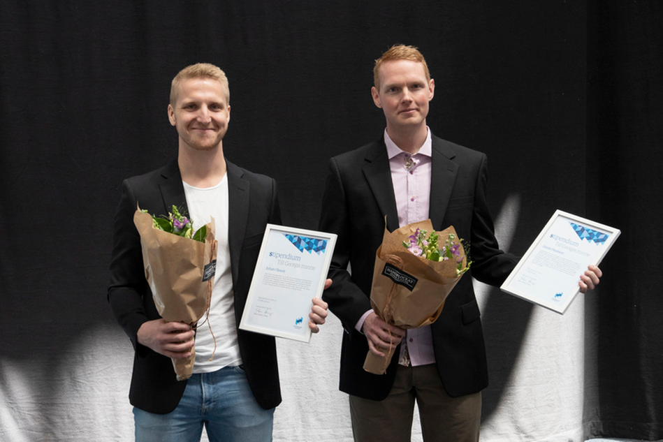 Två manliga studenter mot grå bakgrund håller leende varsitt stipendium samt varsin blombukett.