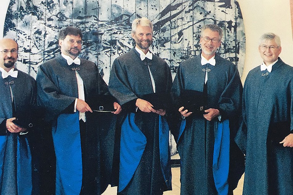 Five people standing next to each other, smiling, all wearing blue capes and formal attire. Photo.