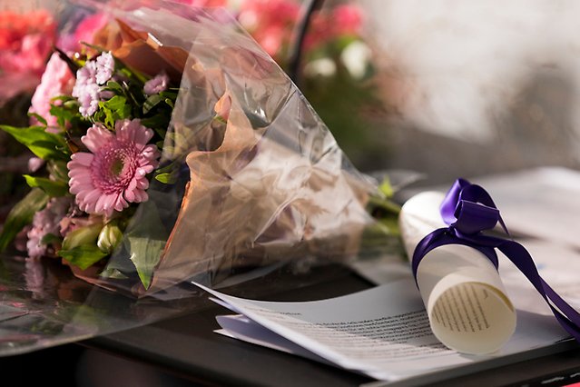 A lying bouquet of flowers on the left. On the right, a diploma with purple ribbons lying on some papers. Photo