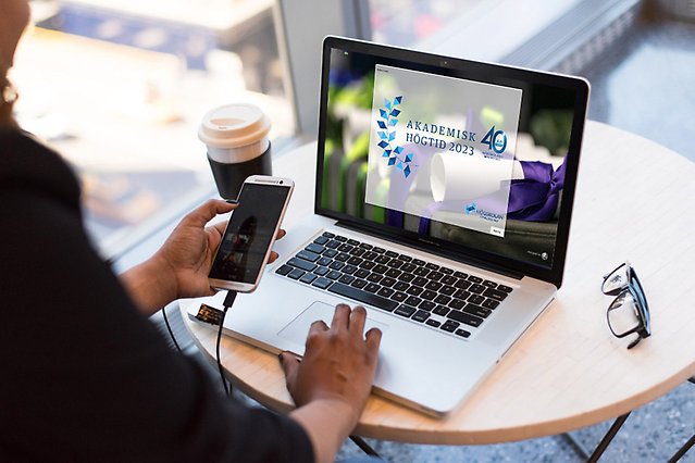 A person sits and writes on a laptop. In the left hand, the person holds a mobile phone. Photo