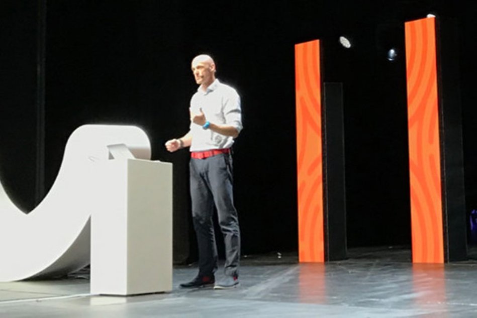 Man standing on a stage talking. Photo.