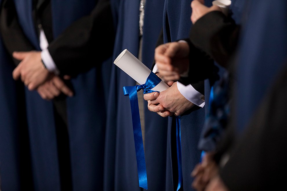 Närbild på händer som håller i ett diplom med blått sidenband. Foto.