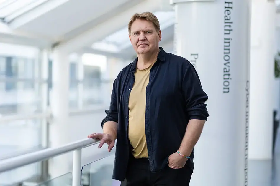 "A person is standing by a railing indoors and looking into the camera. Photo."