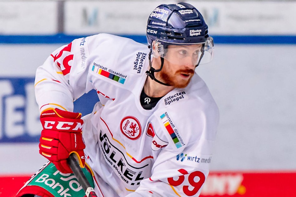 En kille i rött skägg åker på is i full hockeuutrustning.