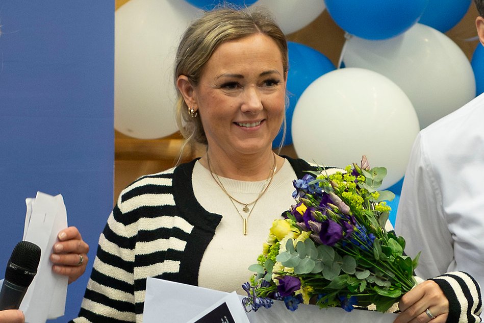 A student standing on a scene and holding a bouquet of flowers and a big check. Photo.