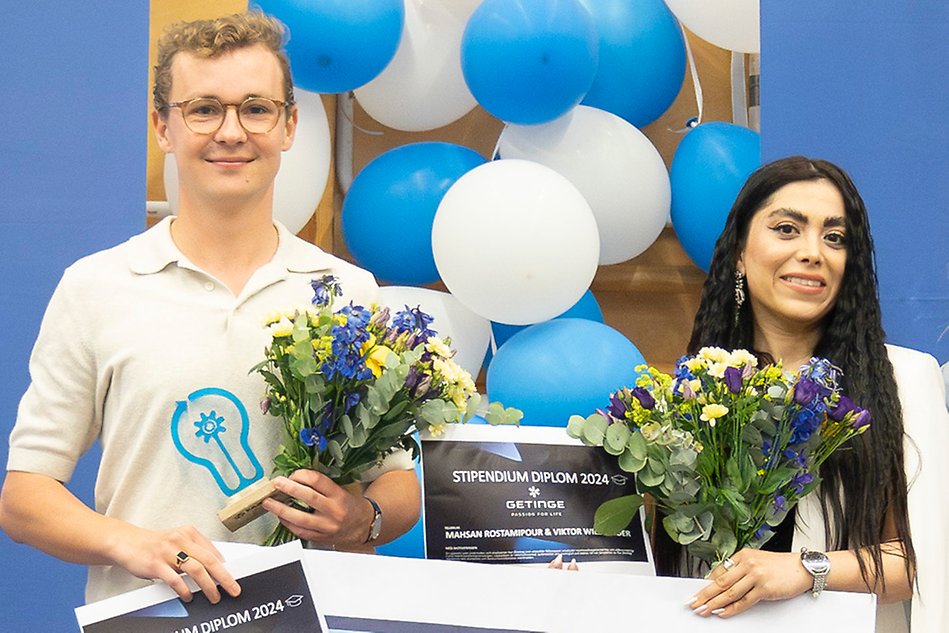 Two students holding bouquet of flowers, statuettes and a check. Photo.