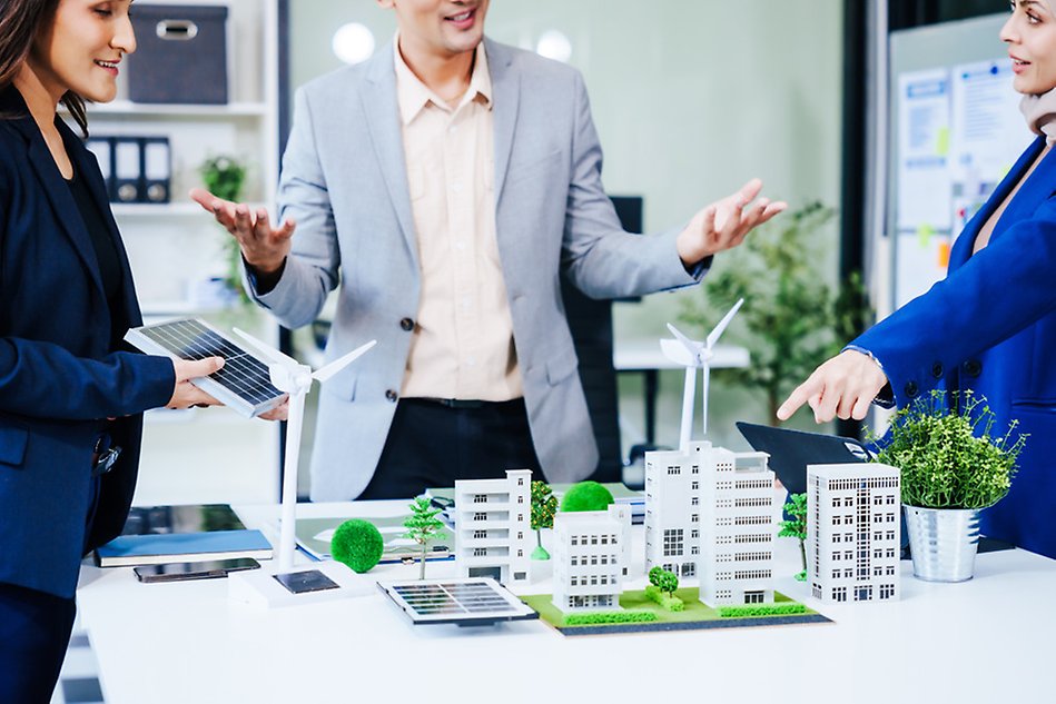 Three people stand around a table with a miniature city on it. Photo.