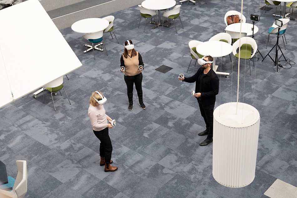 Three persons with VR glasses, big space, grey floor 