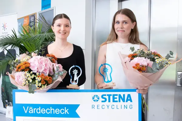 Två personer står bredvid varandra och tittar mot kameran. De håller i blommor och en värdecheck.