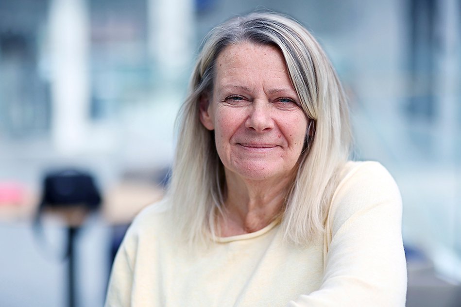 Person som ler och tittar in i kameran. Suddig bakgrund. Foto