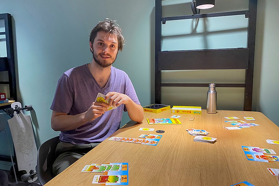 Man in purple t-shirt sitting on chair holding playing cards. 