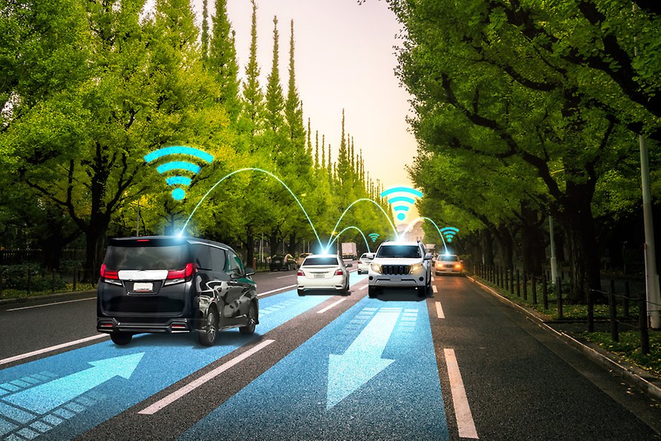 Cars driving down both ways on a road, with wireless network symbols over each car and lines indicating communication between the cars. Photo montage.