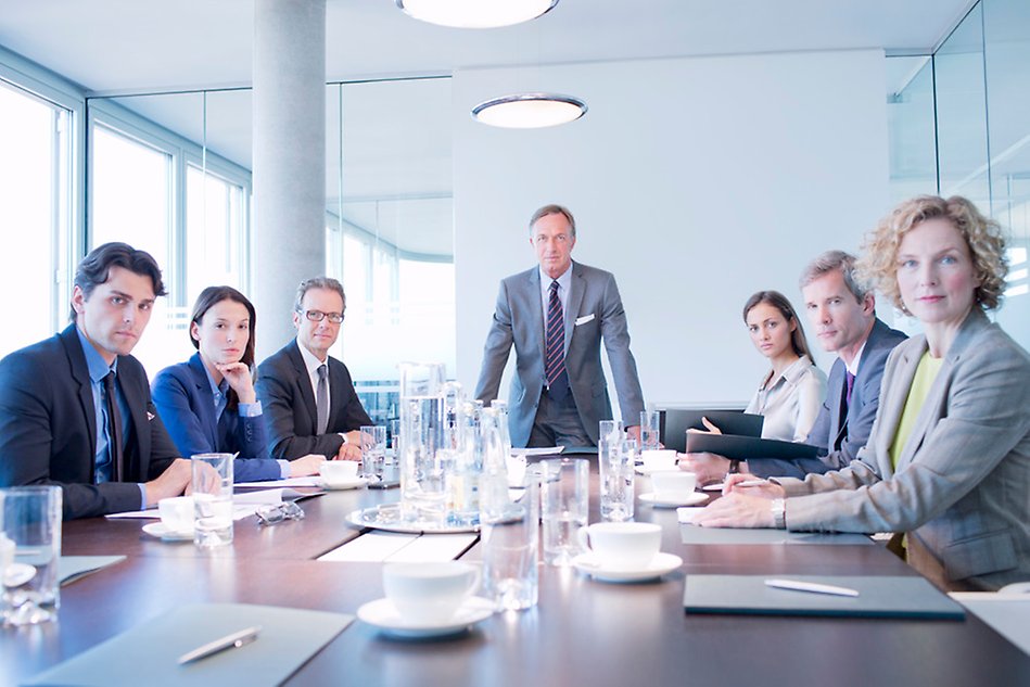 Men and women in suits arond a table. Photo.