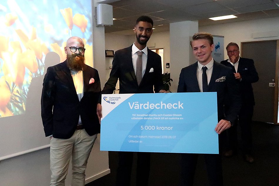 Tre män och en stor check. Alla ler mot kameran. Foto.