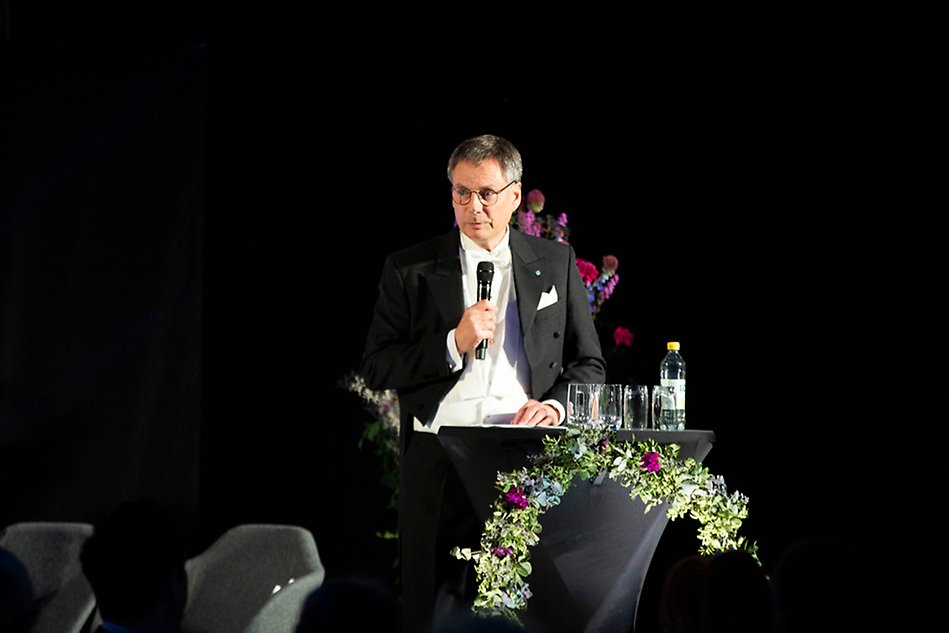 A finely dressed person standing in a lectern. Photography.