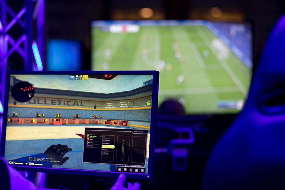 Två skärmar, en i bakgrunden som visar ett fotbollsspel och en i förgrunden som visar ett stridsspel.