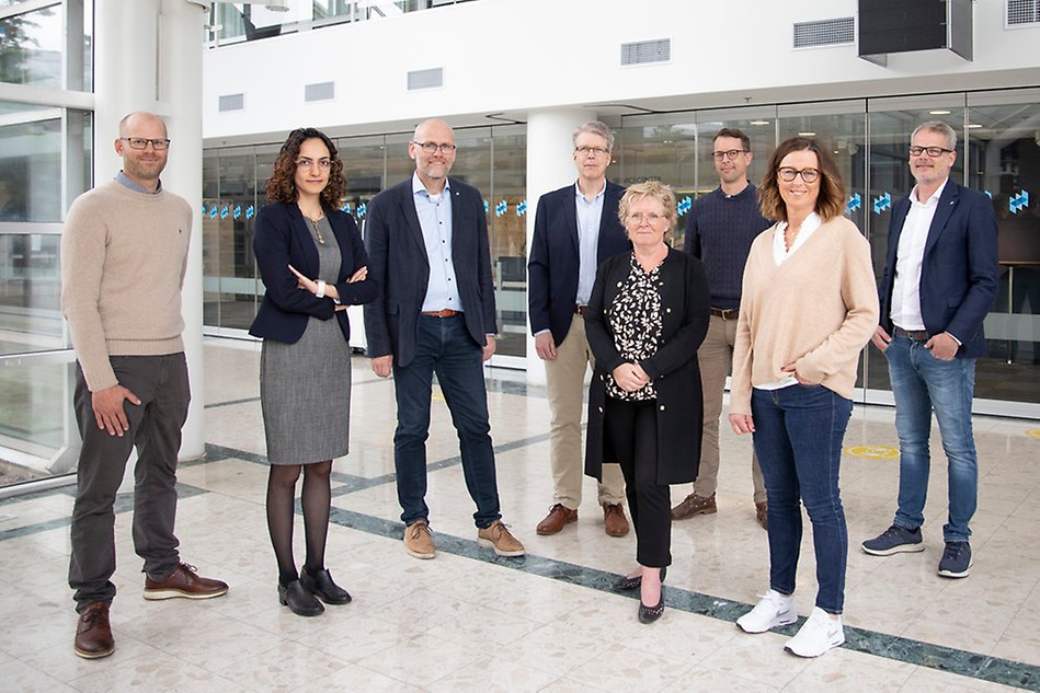 Eight people standing inside a building, looking into the camera.